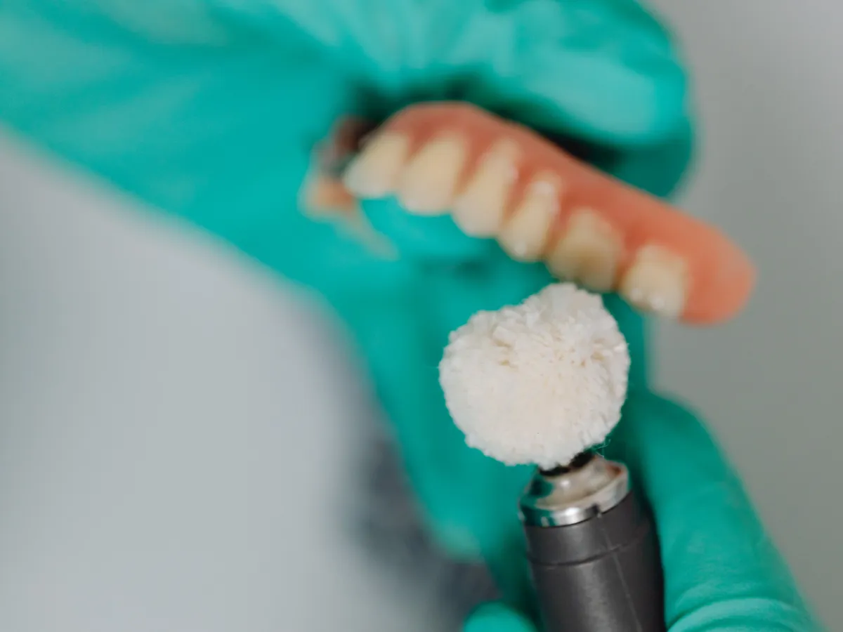 A technician hand-polishing a finished denture with a buffing wheel
